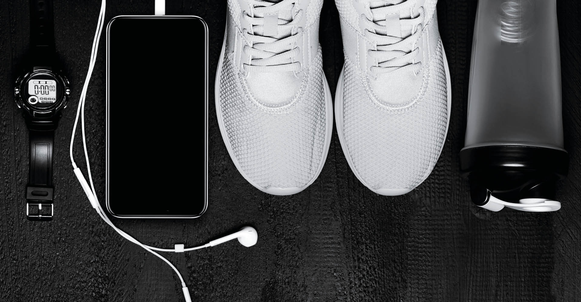 Immagine con rappresentati diversi oggetti: uno borraccia trasparente, un paio di scarpe bianche, un telefono in carica e un orologio.